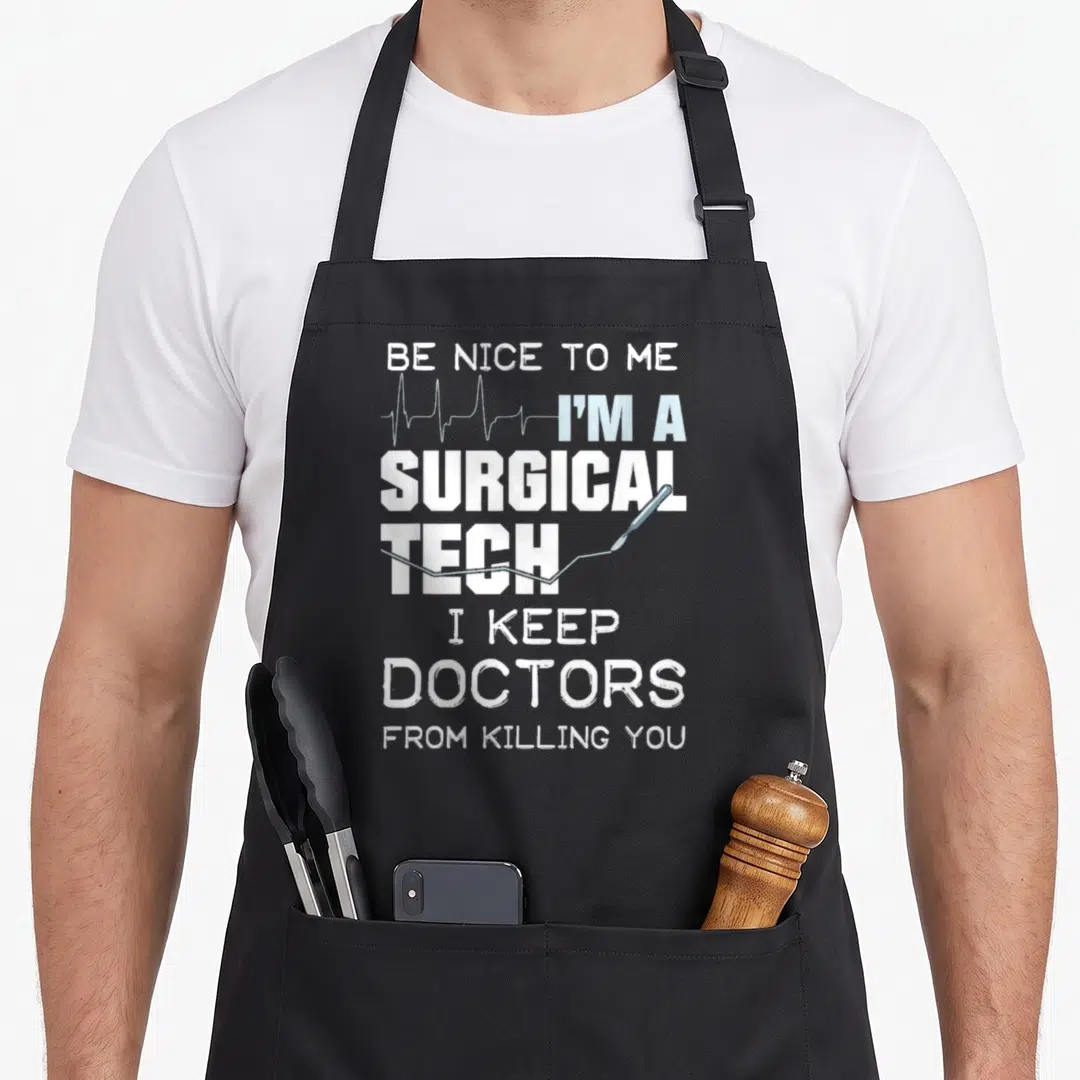 Surgical doctor apron - Stacked white and blue text reading BE NICE TO ME I'M A SURGICAL TECH with EKG line and scalpel — shown on a black cotton canvas apron against a white background