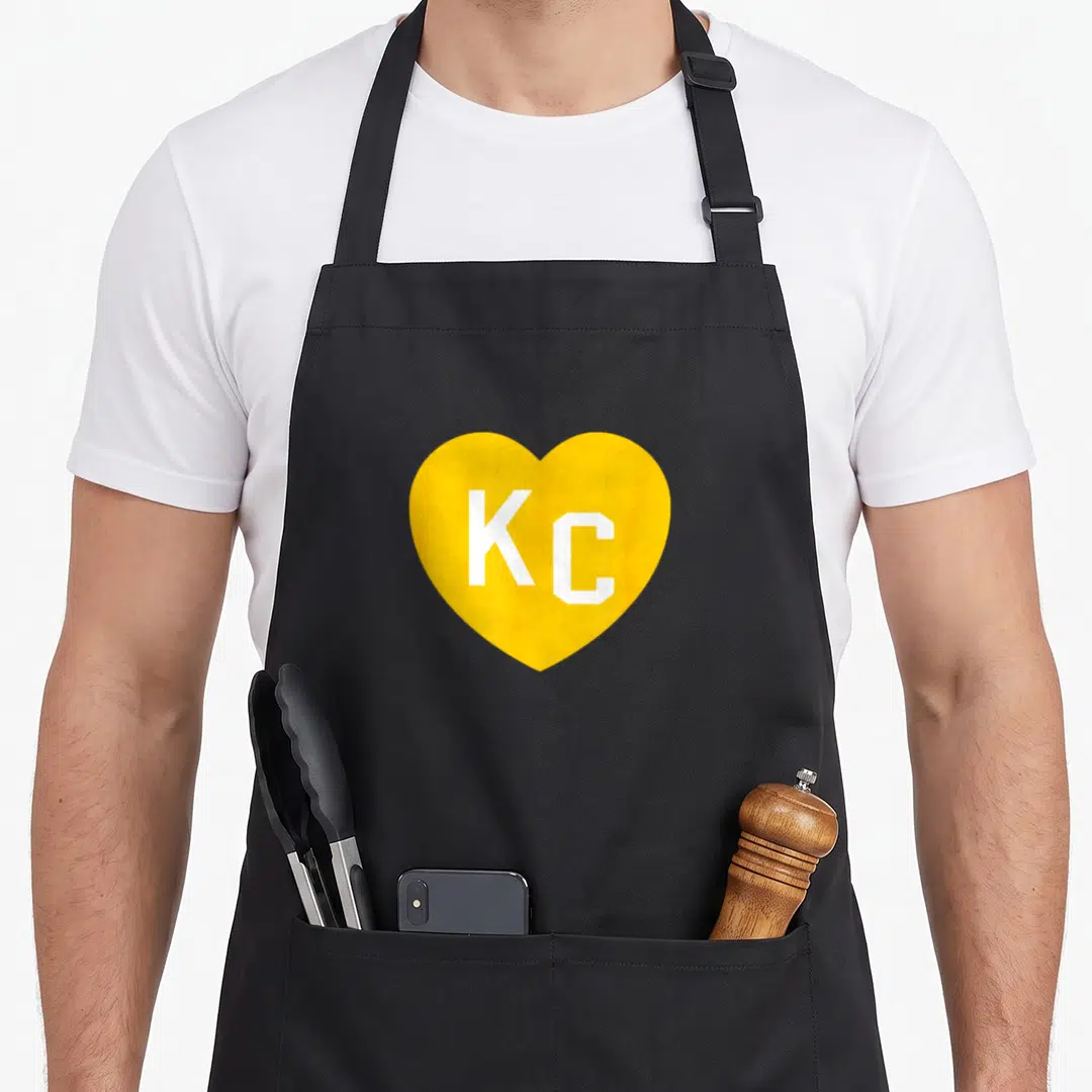 Kansas initial aprons - Yellow heart containing white KC letters on black background — shown on a black cotton canvas apron against a white background