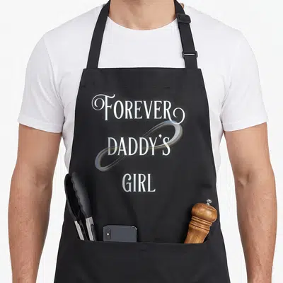 Forever daddy apron - Stacked white text FOREVER DADDY'S GIRL with light blue infinity symbol overlay — shown on a black cotton canvas apron against a white background
