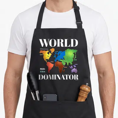 Dominator risk apron - World map with colored territories and WORLD DOMINATOR text — shown on a black cotton canvas apron against a white background