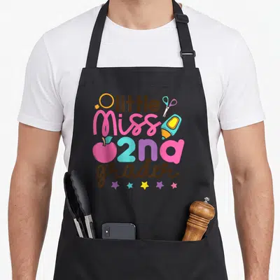 Miss grade 2nd apron - little Miss 2nd grader text surrounded by magnifying glass, scissors, glue stick, apple — shown on a black cotton canvas apron against a white background