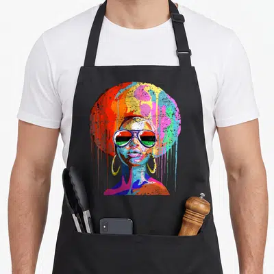 Afro queen apron - Cartoon woman with multicolored afro, dripping paint, and pan-african sunglasses in red yellow blue — shown on a black cotton canvas apron against a white background