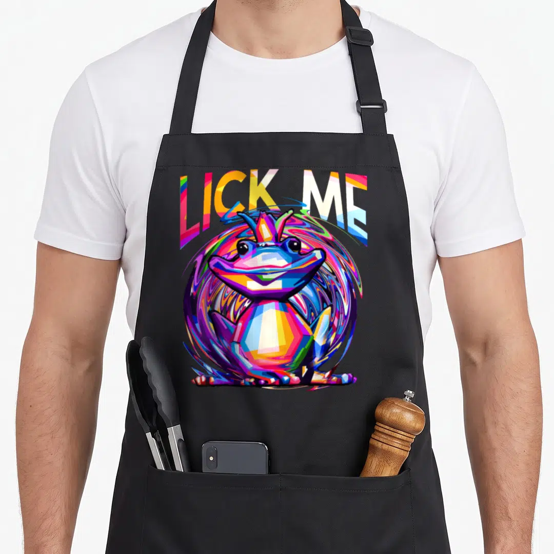 Rave frog aprons - LICK ME text above multicolored cartoon frog with swirling blue, purple, yellow, red, and green — shown on a black cotton canvas apron against a white background