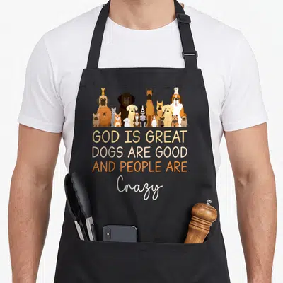 Christian cooking with dog apron - Cartoon dogs above text God Is Great Dogs Are Good And People Are Crazy — shown on a black cotton canvas apron against a white background