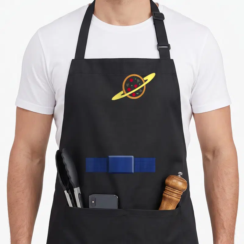 Alien dog breed aprons - Pizza shaped like a planet with yellow ring and blue satellite in cartoon style — shown on a black cotton canvas apron against a white background
