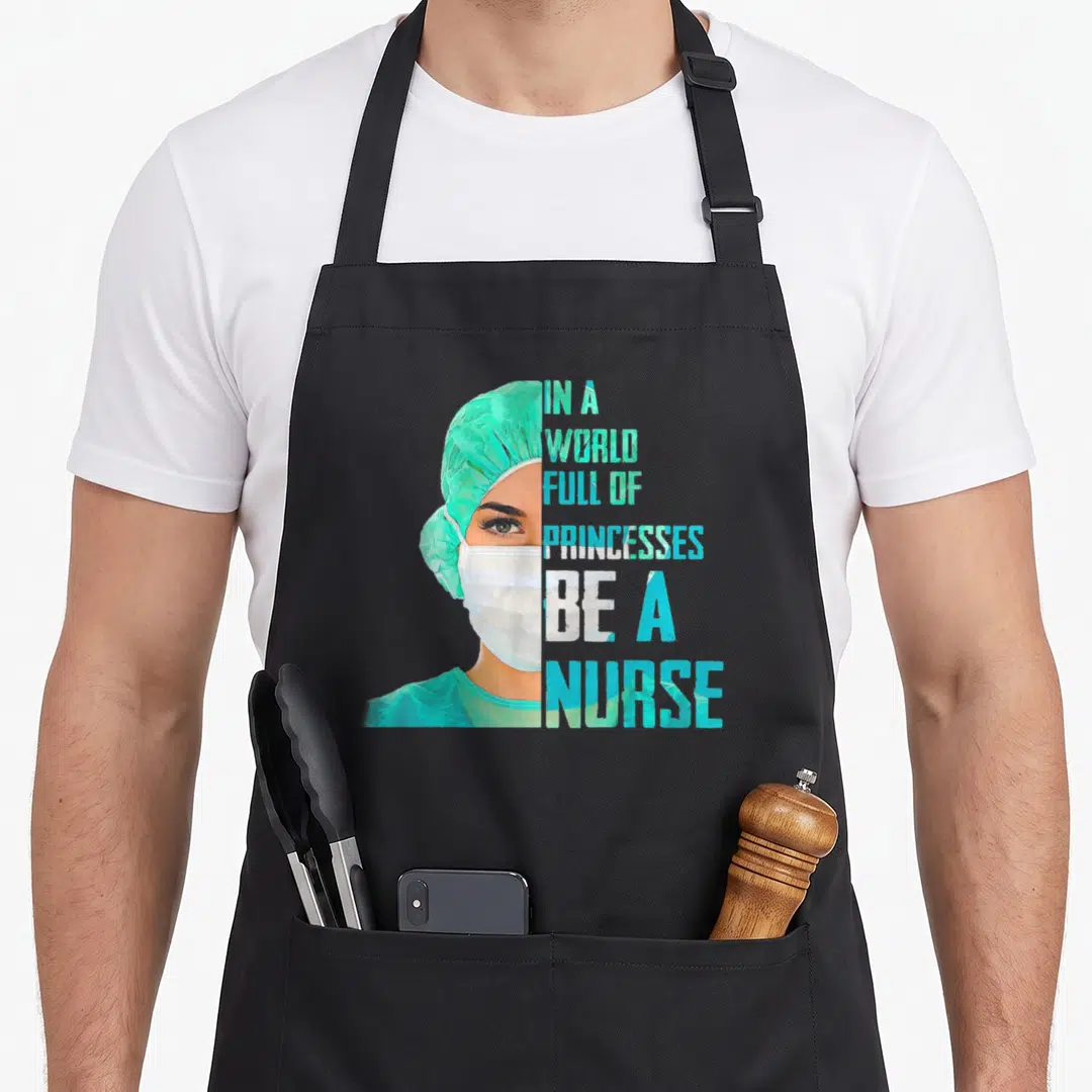Funny princess nurse apron - Realistic nurse portrait with stacked text IN A WORLD FULL OF PRINCESSES BE A NURSE — shown on a black cotton canvas apron against a white background