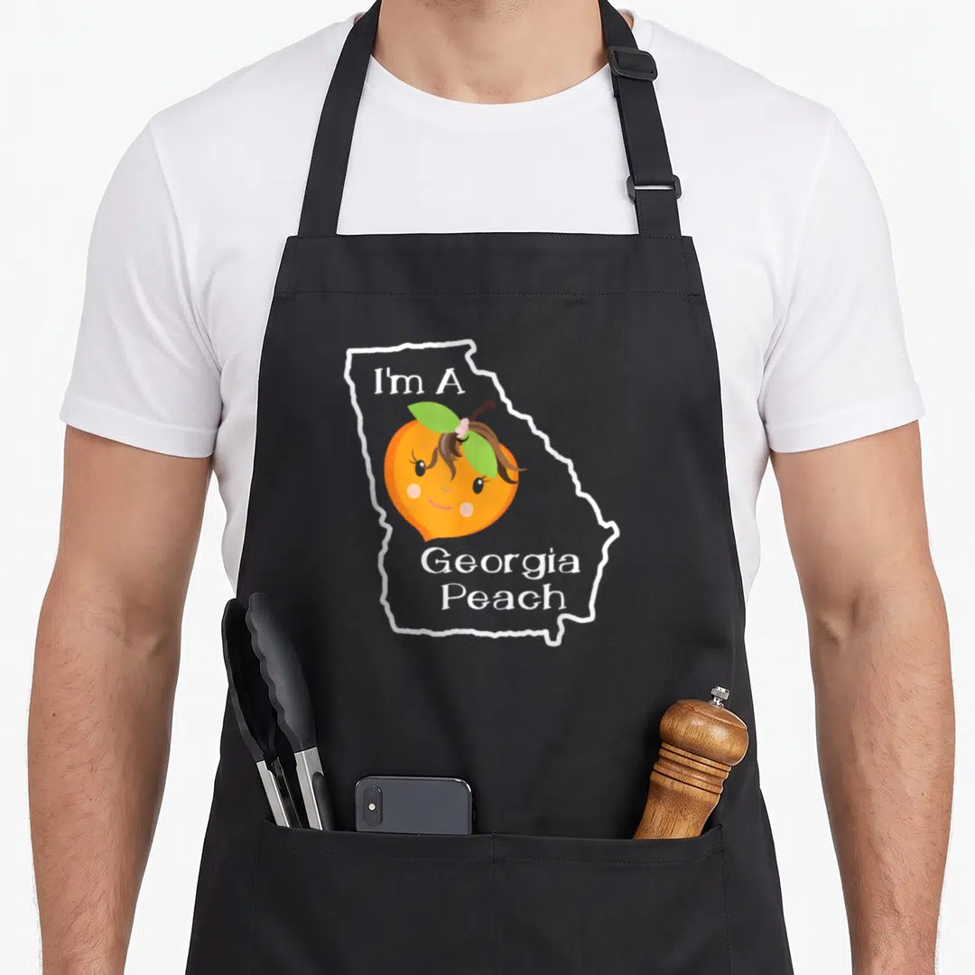 Peach georgia boy apron - Cartoon peach with face inside white Georgia state outline and text — shown on a black cotton canvas apron against a white background