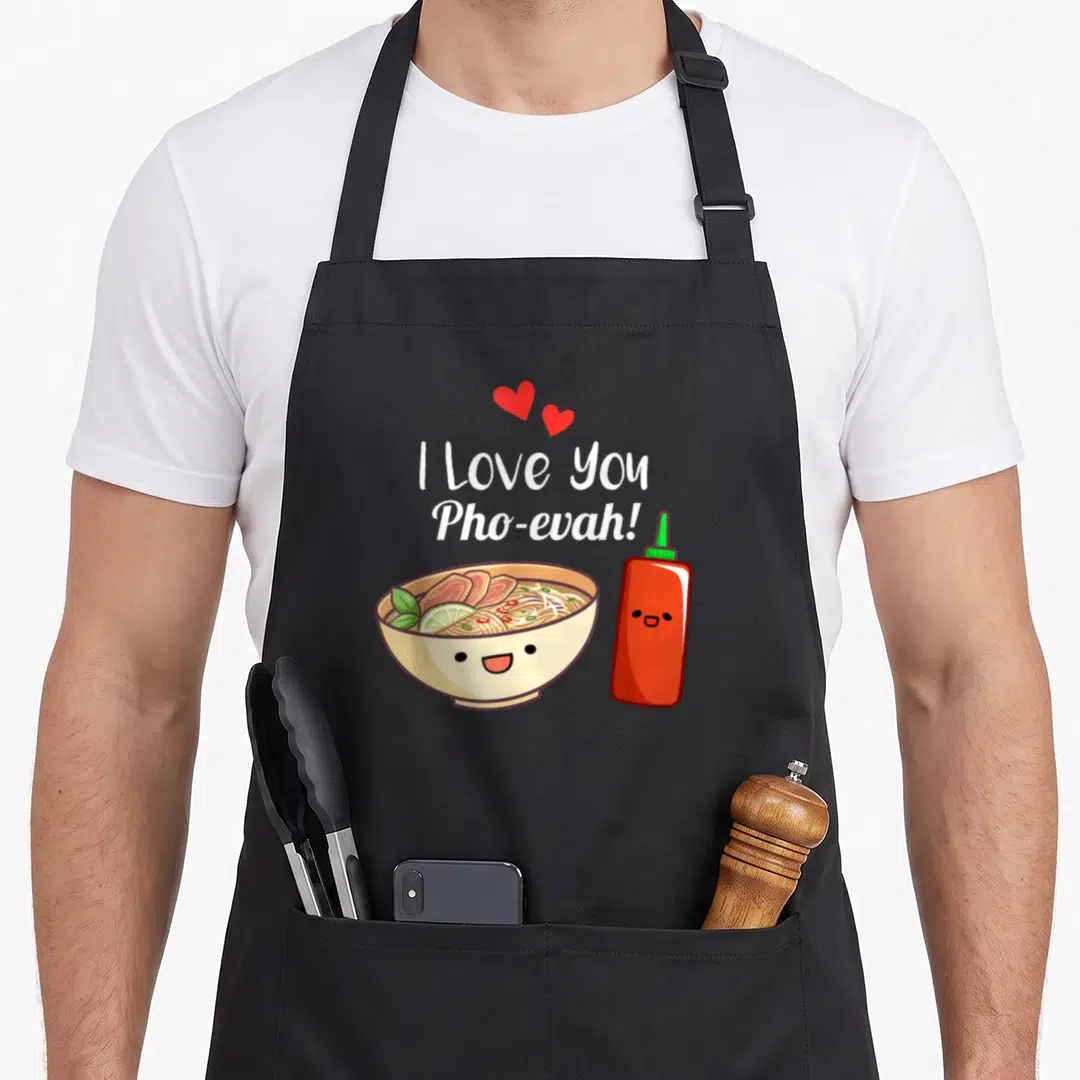Evah pho apron - Cartoon pho bowl and smiling sriracha bottle under I Love You Pho-evah text — shown on a black cotton canvas apron against a white background