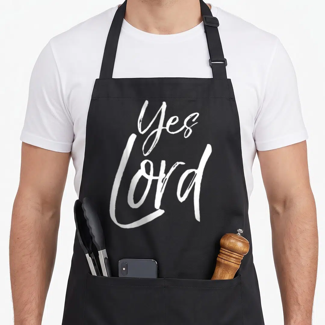 Bold christian apron - White Yes Lord stacked script typography design — shown on a black cotton canvas apron against a white background
