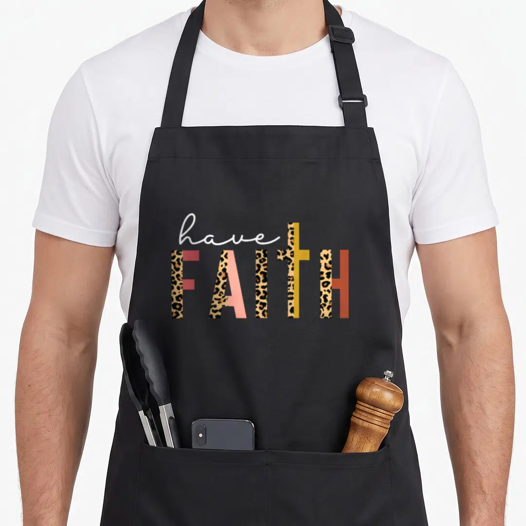 Leopard cross apron - have FAITH text with leopard print fill and cross-shaped T in pink yellow brown colors — shown on a black cotton canvas apron against a white background