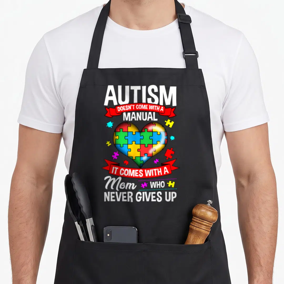 Awareness autism mom apron - Multicolored puzzle heart with red ribbons and white text about autism mom resilience — shown on a black cotton canvas apron against a white background