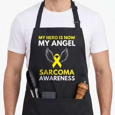 Hero angel ribbon apron - Yellow ribbon with white wings and text My Hero Is Now My Angel Sarcoma Awareness — shown on a black cotton canvas apron against a white background