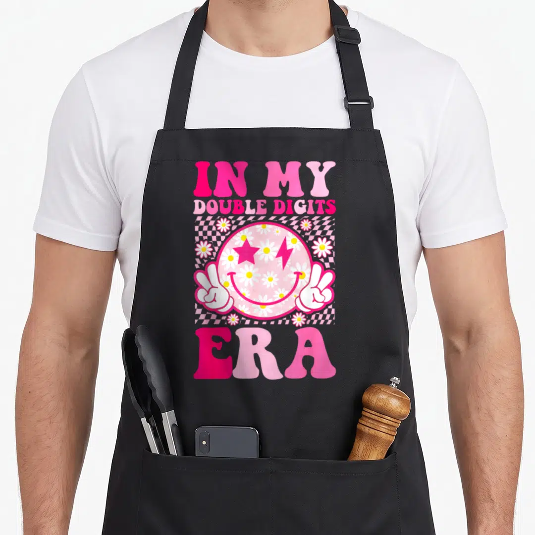 Double custom face apron - Pink smiley face with daisies star lightning bolt and two peace hands on checkerboard — shown on a black cotton canvas apron against a white background