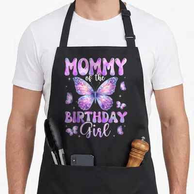Family butterfly aprons - Purple watercolor butterfly design with MOMMY of the BIRTHDAY Girl text and white sparkles — shown on a black cotton canvas apron against a white background