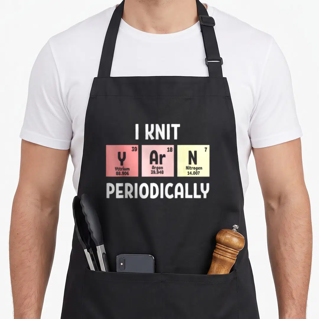 Scientist knitting apron - I KNIT Y Ar N PERIODICALLY text with Yttrium Argon Nitrogen colored squares — shown on a black cotton canvas apron against a white background