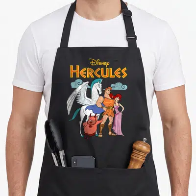 Hercule shot apron - Disney HERCULES text above cartoon hero, Megara, Phil, and Pegasus against light blue clouds — shown on a black cotton canvas apron against a white background
