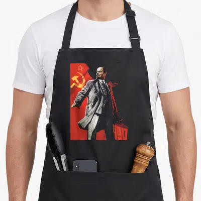 Lenin union aprons - Realistic Lenin standing before red flag with hammer sickle and 1917 text — shown on a black cotton canvas apron against a white background