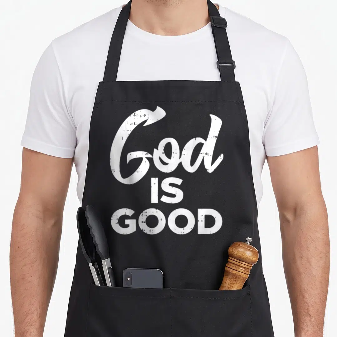 Religion catholic apron - White distressed text reading God IS GOOD stacked vertically — shown on a black cotton canvas apron against a white background