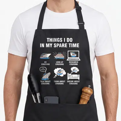 Cruising spare time apron - Six cartoon cruise ship scenes with white text listing spare time activities on a grey — shown on a black cotton canvas apron against a white background