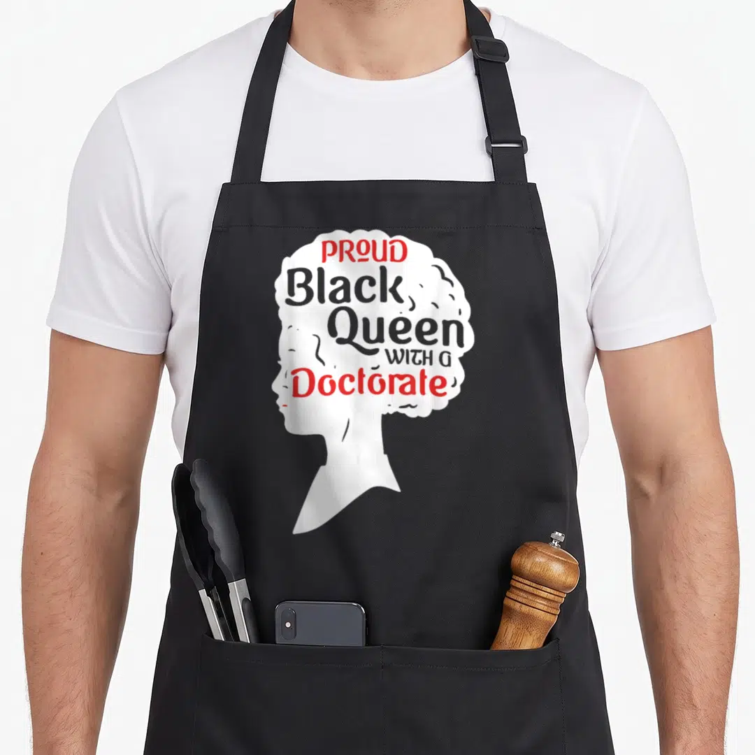 Proud queen apron - White silhouette of a woman's head with red and grey text reading Proud Black Queen With A Doctorate — shown on a black cotton canvas apron against a white background