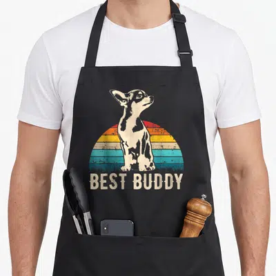 Chihuahueno dog apron - Retro chihuahua standing before striped sunset with BEST BUDDY text below grass line — shown on a black cotton canvas apron against a white background