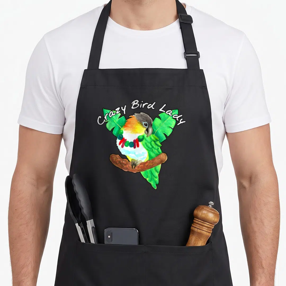 Caique bird apron - Watercolor parrot with beads perched on branch under Crazy Bird Lady text — shown on a black cotton canvas apron against a white background