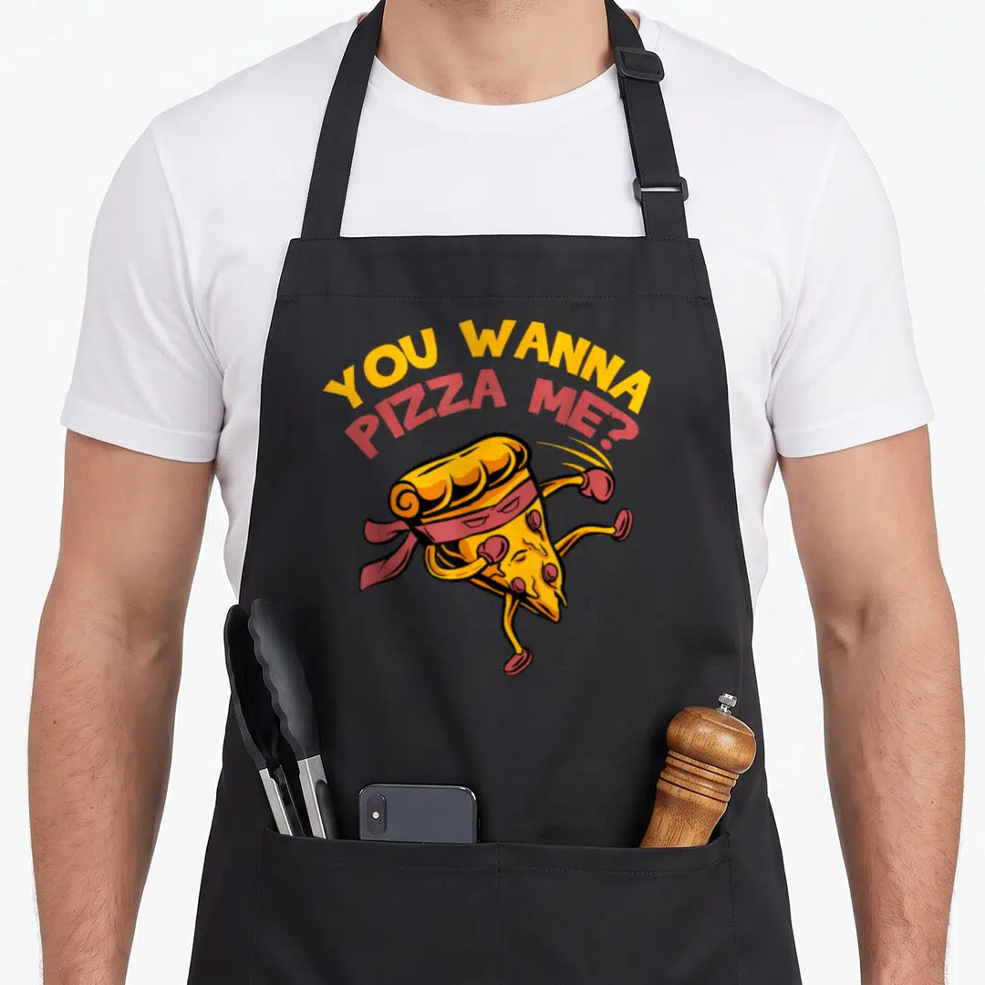 Food pizza apron - Cartoon pizza slice wearing boxing gloves and headband under arched text YOU WANNA PIZZA ME — shown on a black cotton canvas apron against a white background