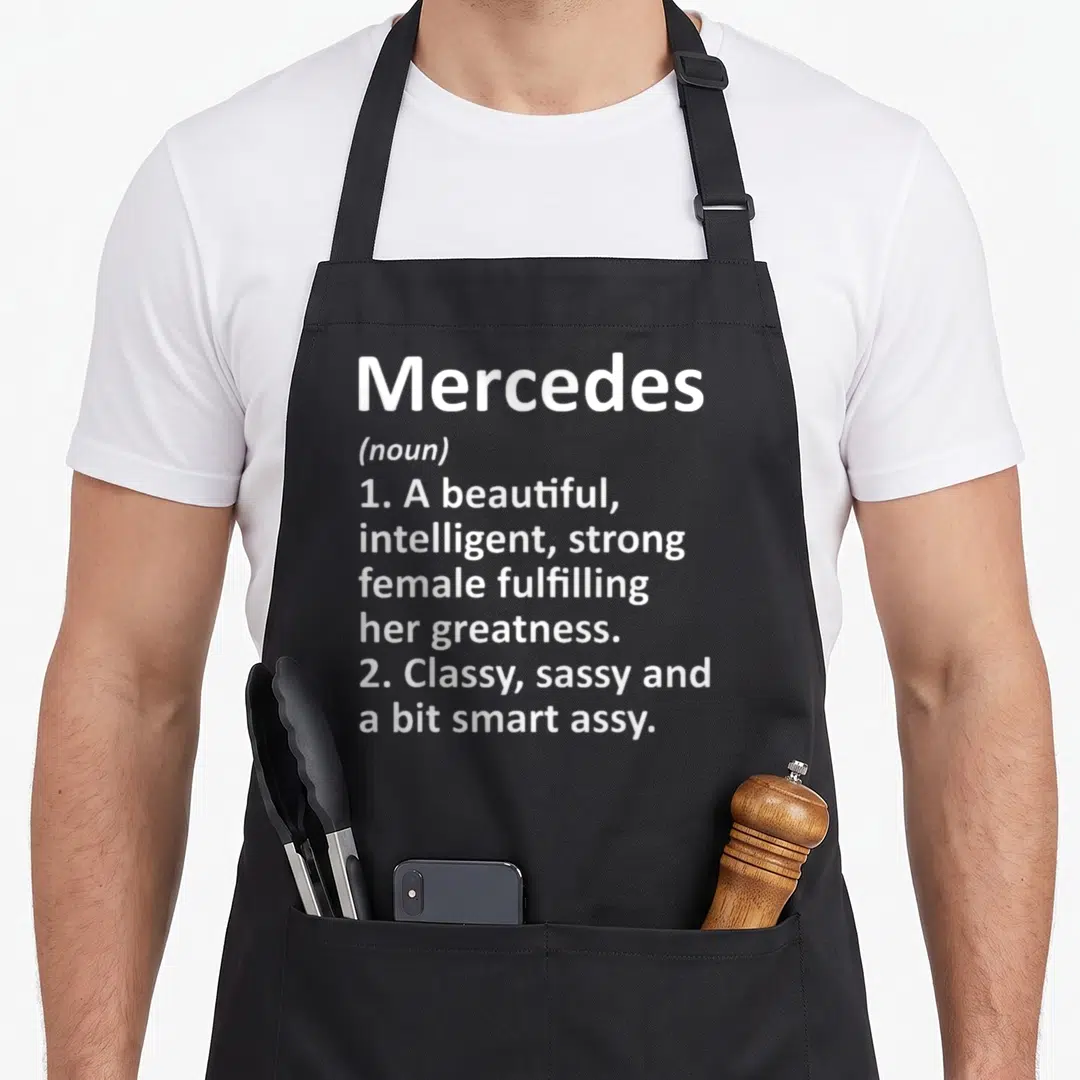 Meaning wife apron - White text defining Mercedes as a beautiful, intelligent, sassy female fulfilling her greatness — shown on a black cotton canvas apron against a white background