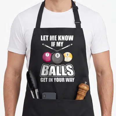 Billiard pool table apron - Crossed white cues above magenta 7, black 8, yellow 9 balls with white pun text — shown on a black cotton canvas apron against a white background