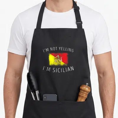 Yelling sicily apron - Distressed flag with triskelion and arched text I'M NOT YELLING I'M SICILIAN — shown on a black cotton canvas apron against a white background