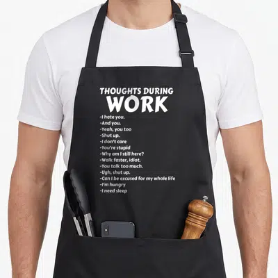 Thought sarcastic apron - White typography listing 15 sarcastic work thoughts like I hate you and I need sleep on black — shown on a black cotton canvas apron against a white background