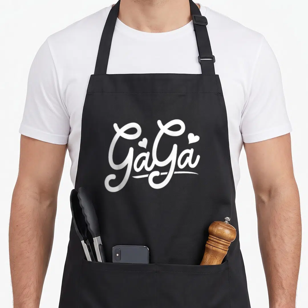 Grandchildren novelty apron - White script text reading GaGa with two hearts above the letters — shown on a black cotton canvas apron against a white background