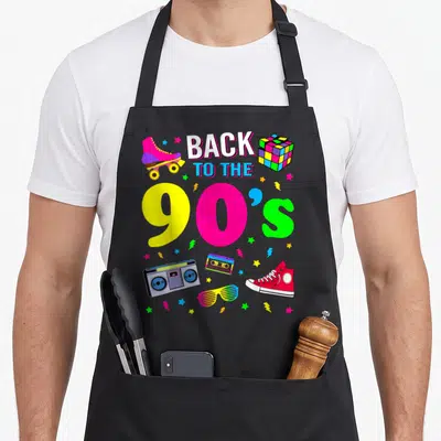 Ninety 90s apron - Back to the 90s text with boombox, roller skate, and colorful stars in cartoon style — shown on a black cotton canvas apron against a white background