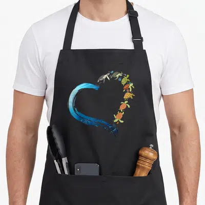 Sea tortoise apron - Seven sea turtles and blue water splash forming a heart shape in cartoon style — shown on a black cotton canvas apron against a white background