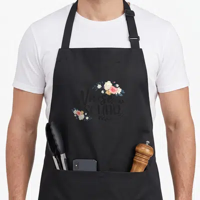 Squad nursing student apron - Nurse SQUAD text with pink and blue-grey floral clusters in corners — shown on a black cotton canvas apron against a white background