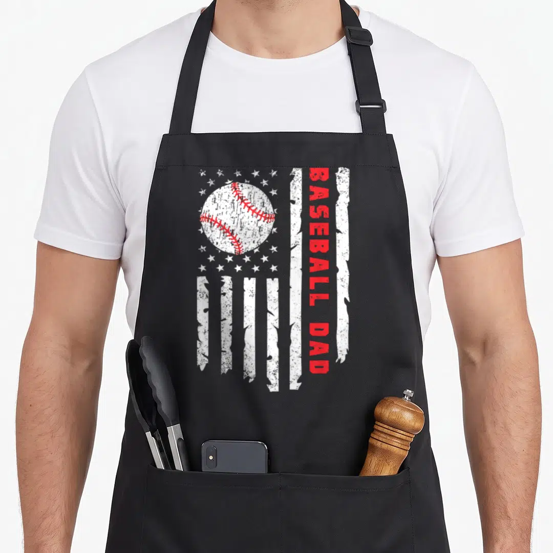 Baseball flag father day apron - Distressed flag design with white baseball, red vertical text BASEBALL DAD, and white — shown on a black cotton canvas apron against a white background