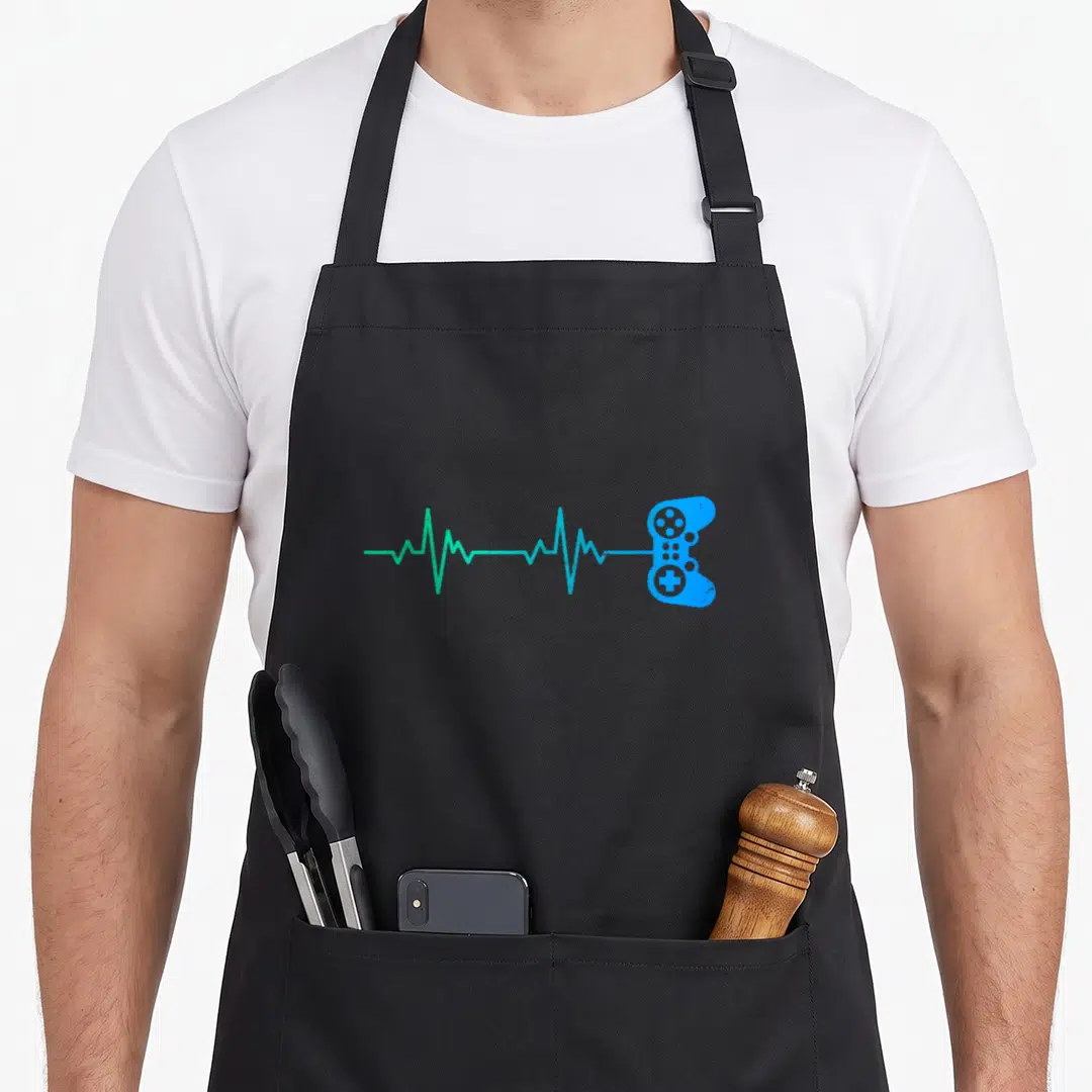 Heartbeat game aprons - Teal heartbeat line connecting to a blue game controller silhouette — shown on a black cotton canvas apron against a white background