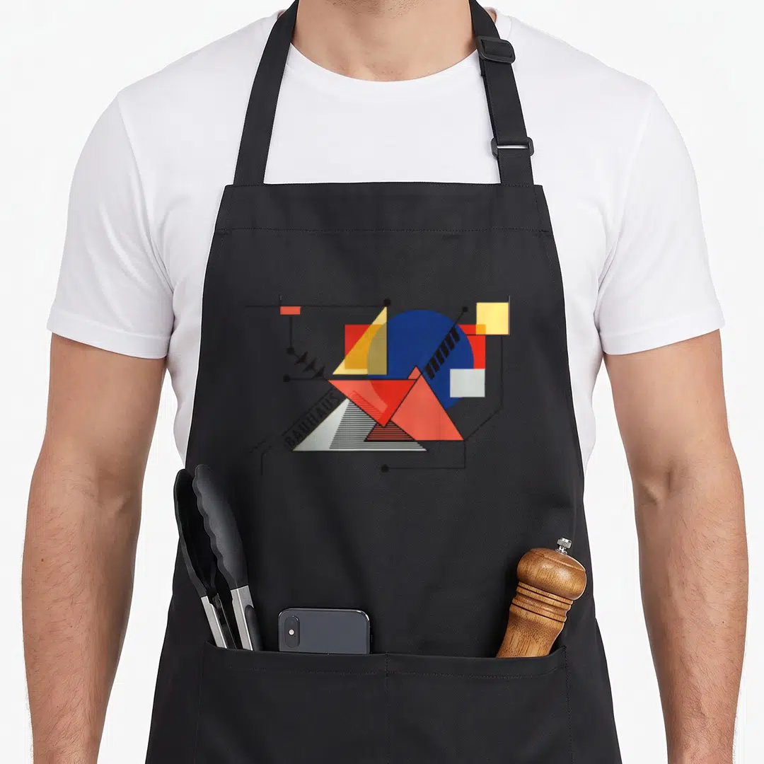 Bauhaus lover artwork apron - Abstract geometric shapes in blue red yellow and black with BAUHAUS text on a white — shown on a black cotton canvas apron against a white background