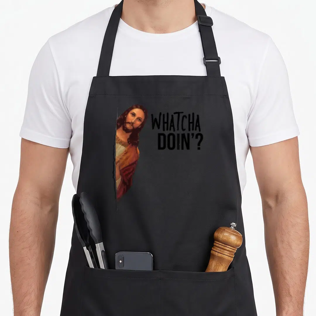 Jesus watching meme apron - Cartoon Jesus peeking through a tear next to black stacked text reading whatcha doin — shown on a black cotton canvas apron against a white background