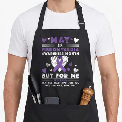 May ribbon apron - Purple ribbon over white heart with text listing all months for fibromyalgia awareness — shown on a black cotton canvas apron against a white background