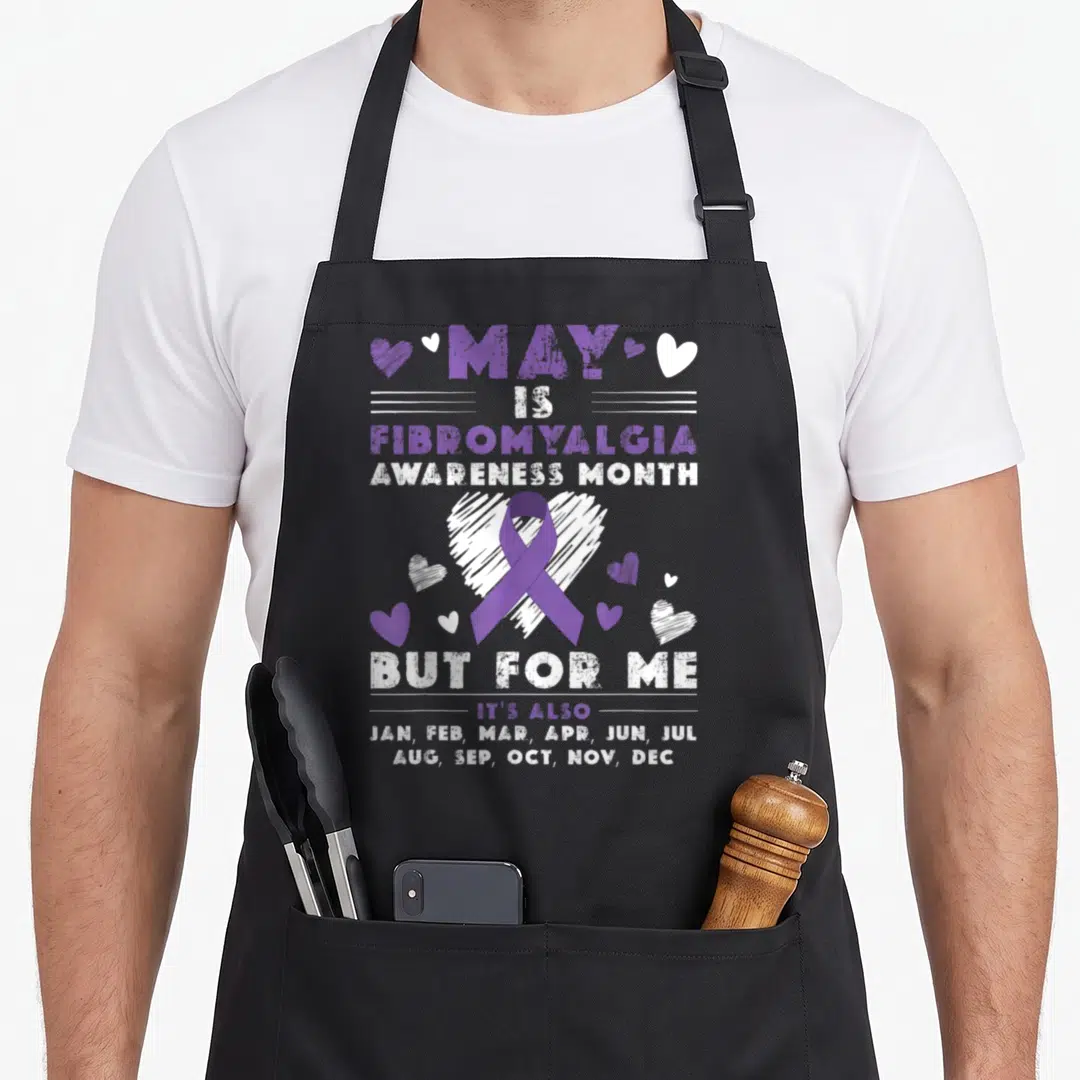 May ribbon apron - Purple ribbon over white heart with text listing all months for fibromyalgia awareness — shown on a black cotton canvas apron against a white background