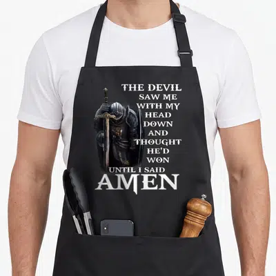 Hed devil's apron - Knight in black armor with sword beside stacked white prayer text ending in silver AMEN — shown on a black cotton canvas apron against a white background