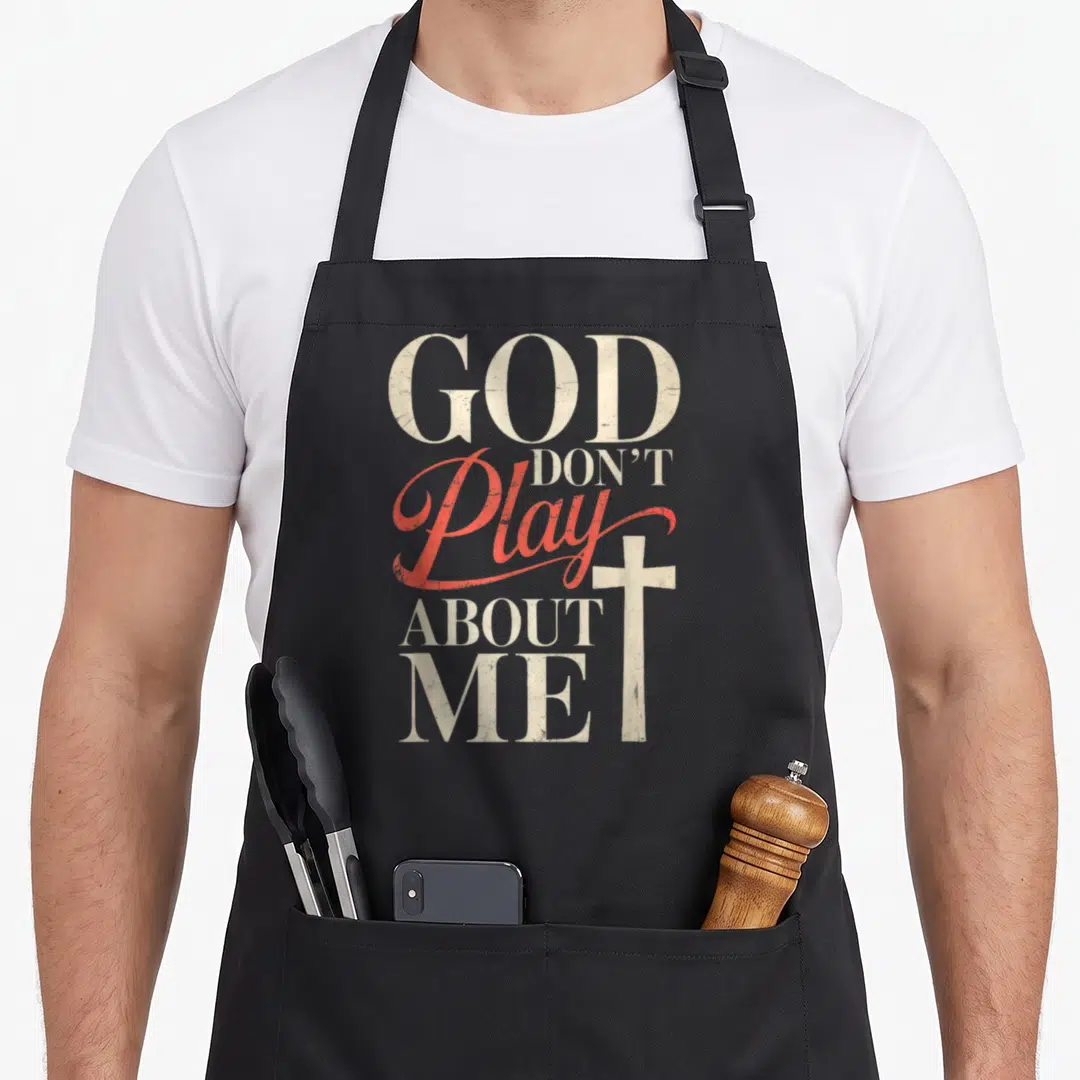 Vintage god play about apron - Stacked text GOD DON'T Play ABOUT ME with red script and distressed off-white cross — shown on a black cotton canvas apron against a white background