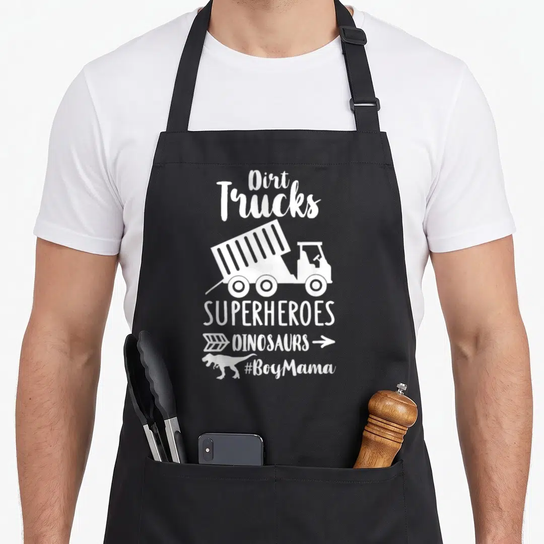 Superheroe truck apron - White dump truck and dinosaur silhouette with stacked text reading Dirt Trucks Superheroes — shown on a black cotton canvas apron against a white background