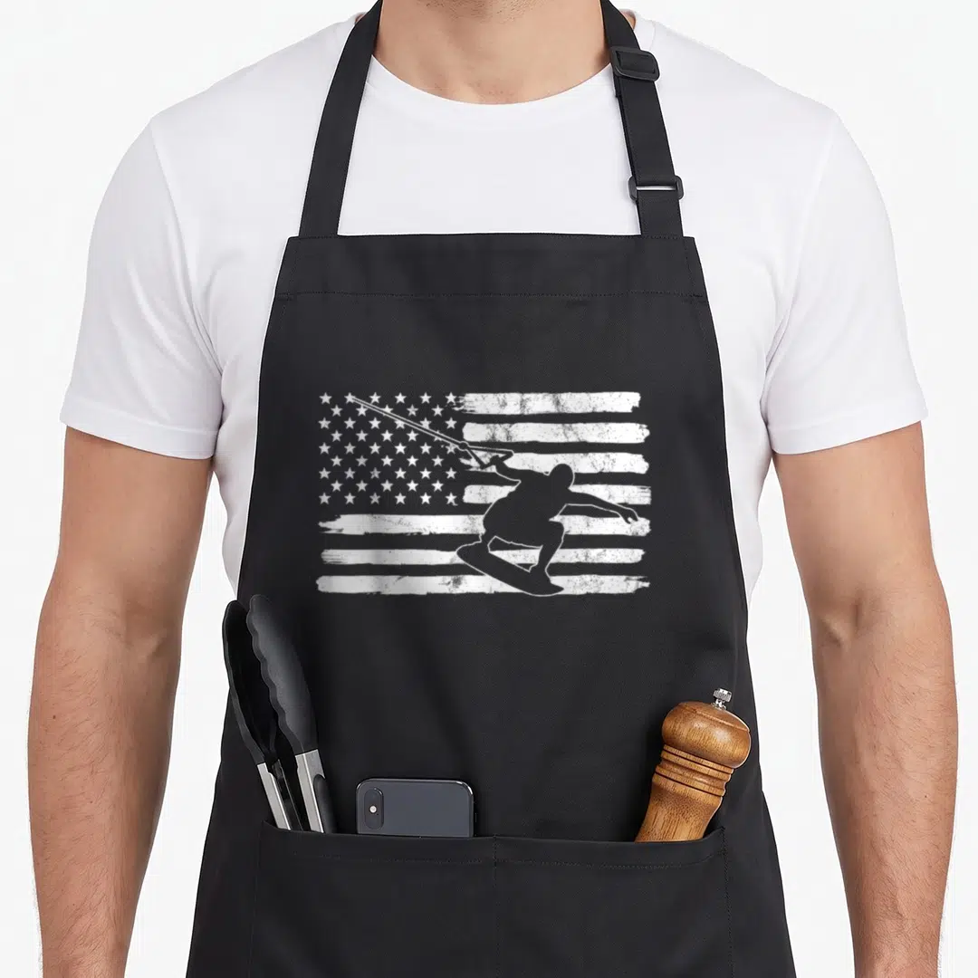 Wakeboarding 4th of july apron - White wakeboarder silhouette over distressed USA flag pattern — shown on a black cotton canvas apron against a white background
