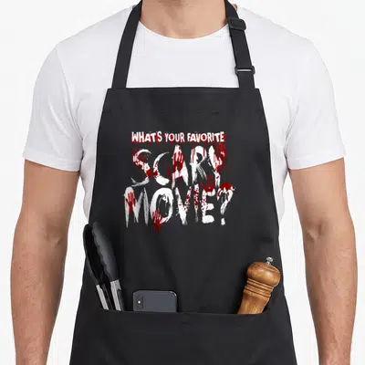 Scary horror movie apron - White text reading WHAT'S YOUR FAVORITE SCARY MOVIE covered in red blood splatters — shown on a black cotton canvas apron against a white background