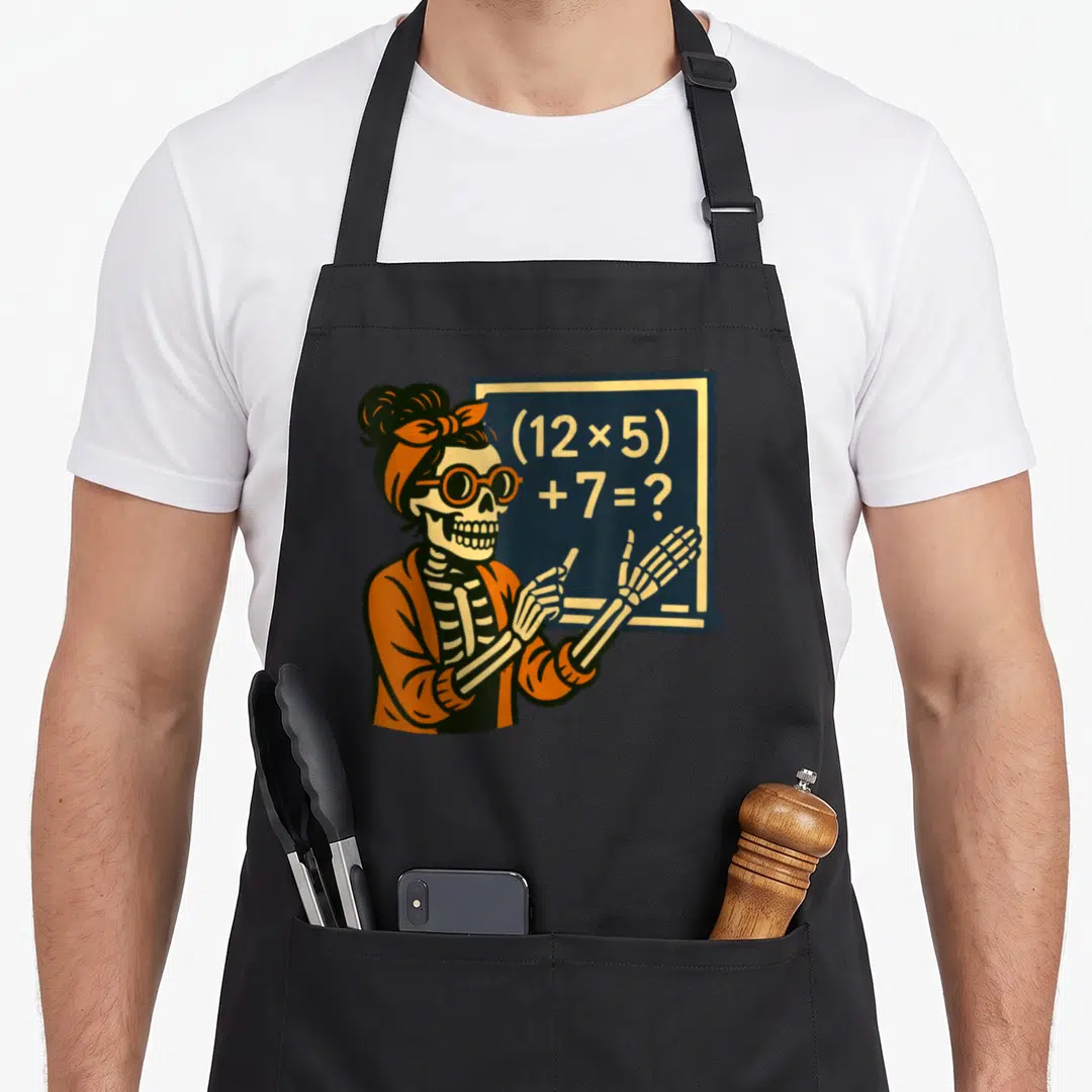 Halloween teacher apron - Cartoon skeleton teacher pointing at chalkboard equation (12x5) +7= in orange and blue — shown on a black cotton canvas apron against a white background