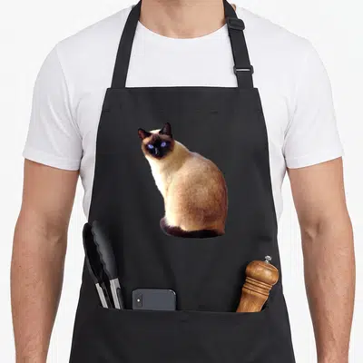Animal cute cat aprons - Photo of a sitting Siamese cat with blue eyes and beige brown fur — shown on a black cotton canvas apron against a white background