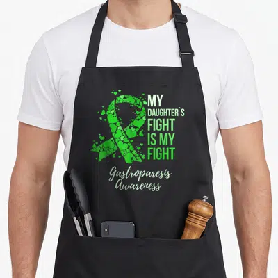 Daughter gastroparesis awareness apron - Green ribbon made of hearts next to stacked text reading My Daughters Fight Is — shown on a black cotton canvas apron against a white background