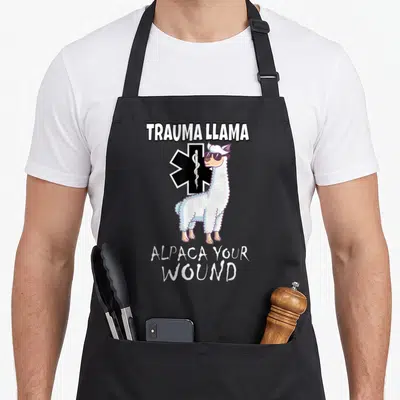 Trauma alpaca apron - Cartoon llama with sunglasses in front of Star of Life and text TRAUMA LLAMA ALPACA YOUR WOUND — shown on a black cotton canvas apron against a white background